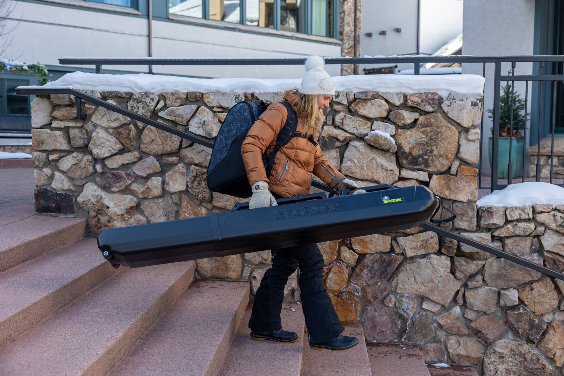 Skier carrying a Sportube hard case down snowy steps